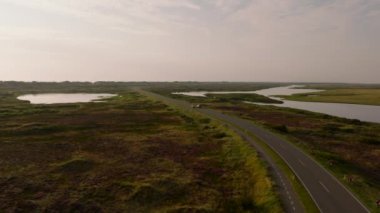 Yol boyunca giden bir arabanın hava görüntüsü. Yol iki taraftan da suyla çevrili, Ringkobing Fjord bir tarafta ve Kuzey Denizi diğer tarafta..