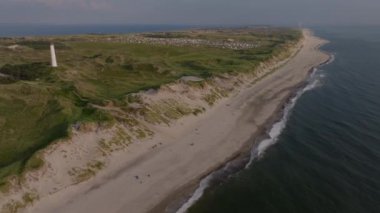 Havadan bakıldığında, berrak ve güneşli bir gökyüzünün altında manzaralı bir deniz feneri, antika bir köy ve uçsuz bucaksız Kuzey Denizi 'nin yer aldığı canlı ve kumlu bir sahil şeridi görülüyor..