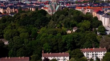 Stockholm şehrindeki kameralar binaların ve yemyeşil ağaçların geniş bir manzarasını gösteriyor. Sofya Kilisesi merkezde tanınıyor.