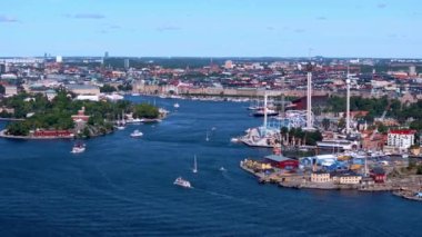 Botlar Stockholm limanının su yollarında geziniyor, canlı şehir manzarasını sergiliyorlar. Eğlence parkı Grona Lund sağda belirgin bir şekilde duruyor ve hareketli atmosfere ekliyor..
