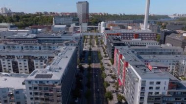 Kamera, modern binaları, ofisleri ve apartmanları ile Hammarby Sjostad bölgesinde ilerliyor. Modern bir mahallede büyük caddeler ve bitki örtüsü.