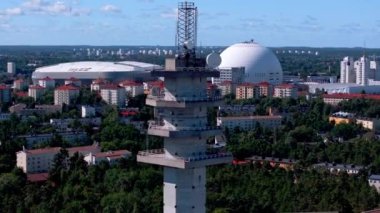 Stockholms kentsel manzarasının üzerinde Ericsson Globe ve Tele2 arenası gibi işaretleri vurgulayan bir iletişim kulesini gösteren hava görüntüsü.