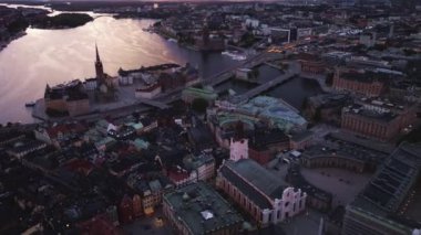 Stockholm şehir merkezinde güneş batıyor. Suyu yansıtıyor. Çerçevede Riddarholmen Kilisesi ve köprüsü yer alıyor.