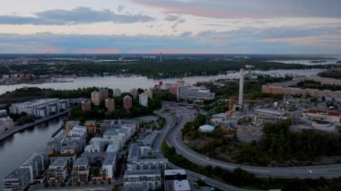 Stockholm şehri alacakaranlıkta ufuk çizgisinde. Arabalar yol boyunca köprüye doğru gidiyor, renkli gökyüzü suya yansıyor..