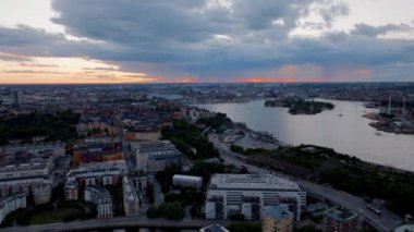 Stockholm şehrinin silueti canlı bir günbatımının ılık renklerini yansıtıyor. Bulutlar toplanıyor, gölgeler şehrin aşağısına düşüyor..