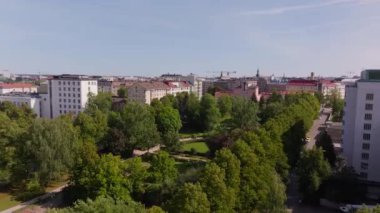 Helsinki, Finlandiya 'daki canlı bir parkı gösteren hava görüntülerinde, açık mavi gökyüzünün arka planına karşı gür ağaçlar ve çağdaş binalar sergilenmektedir..