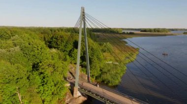 Güneşli bir yaz gününün keyfini çıkaran insanların Helsinki 'nin varoşlarındaki bir köprüde yürüyüş ve bisiklet sürüşünün havadan görüntüsü. Köprü ve mavi suyun etrafını saran yemyeşil ağaçlar.