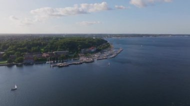 Almanya 'nın Kiel kentinin her yerinde renkli binalar, yemyeşil bir orman ve canlı bir limanda demirlemiş tekneler görülüyor. Şehir manzarası ve şehir manzarası gözler önüne seriliyor..