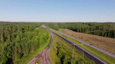 Çevresi yemyeşil bir ormanla çevrili hava manzaralı araçlar otoban boyunca sürüyor. Canlı manzara, yaz yolculuğunun güzelliğini vurgular..