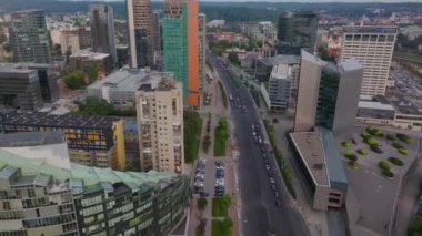 Litvanya 'nın Vilnius kentinde bulutlu bir gökyüzü altında yemyeşil ağaçlarla çevrili, çok şeritli bir otoyolda modern binaları ve akan trafiği hava manzaraları sergiliyor..