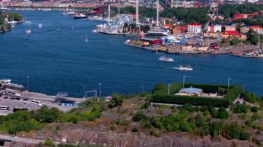Stockholm limanında renkli Grona Lund eğlence parkı ve şehrin ufuk çizgisi manzaralı tekneler kamera gibi hareket ediyor..