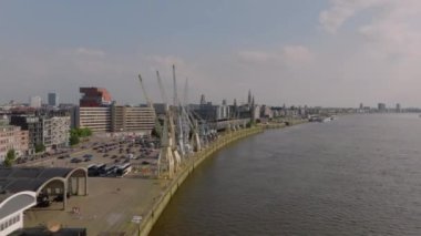 Kamera Antwerp ufuk çizgisini, iskele vinçlerini ve Scheldt Nehri 'ni gösteriyor. Bazı turistler ve yerliler güneşli yaz gününün tadını çıkarıyorlar..