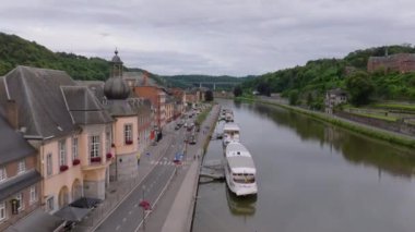 Meuse nehrinin Belçika 'daki Dinant şehrinin evleri ve binaları arasında akan hava manzarası. Birkaç tekne kıyıya demirlemiş..