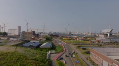 Antwerp 'te depoları ve vinçleri olan bir liman alanını bölen araçlar yolda ilerliyor. Rüzgar türbinleri ve bir müze gemisi uzaktan görülebiliyor..
