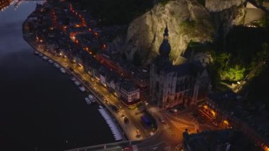Gece Belçika 'da Dinant' ın hava manzarası. Aydınlatılmış Kolej Kilisesi karanlık binaların arasında duruyor. Arabalar köprüden geçiyor..
