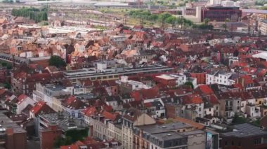 Kentsel manzara, ikonik kırmızı çatılarıyla Brüksel 'i vurguluyor. Güneşli bir yaz gününde, bir tren uzak raylar boyunca süzülür, canlı atmosferi güçlendirir..