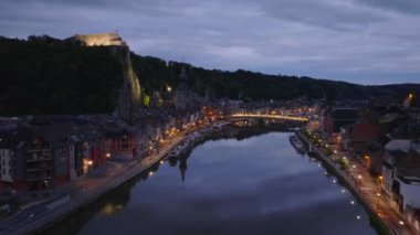 Havadan bakıldığında, Belçika 'nın Dinant kentinin ışıldayan manzarası alacakaranlıkta Meuse nehrinin üzerinde yavaşça süzülerek kayalıkların tepesindeki pitoresk mimariyi ve ikonik Hisar' ı vurguluyor..