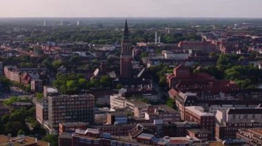 Almanya 'nın Kiel kentindeki binaları ve caddeleri aydınlatan güneş ışığı, canlı şehir manzarasının üzerinde yükselen yüksek bir kilise kulesini vurguluyor..