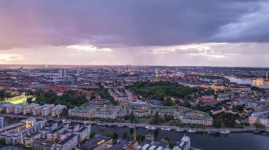 Alacakaranlık sırasında nefes kesen Stockholm ufuk çizgisinin hava hiperhızlandırıcı görüntüsü dramatik bulutlar ve deniz yüzeyine yansıyan canlı şehir ışıklarını gösteriyor..