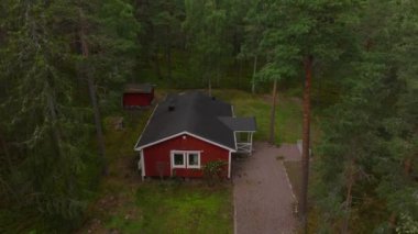 Siyah çatılı kırmızı İsveç evi yemyeşil ormanlarla çevrili bir açıklıkta duruyor. Sakin ortam, yaz boyunca kırsal hayatın güzelliğini gözler önüne seriyor..