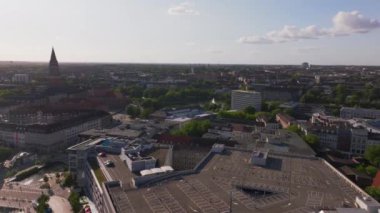 Almanya 'nın Kiel kentinin hava manzarası, bir kilisenin önde gelen çan kulesinin yanında canlı bir şehrin ufuk çizgisini sergiliyor, kentsel mimari ve manzaralı rıhtımın karışımını vurguluyor..