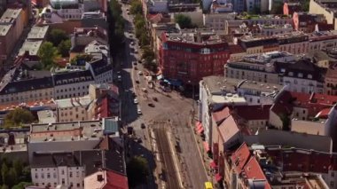 Berlin, Almanya 'da işlek bir kavşaktan geçen sarı bir tramvayın hava görüntüsü. Arabalar ve yayalar güneşli bir günde hareketli şehir manzarasında yol alırlar..
