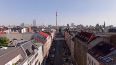 Berlin 'deki işlek caddelerde, İskenderplatz' ın ikonik Fernsehturm 'u berrak mavi gökyüzüne doğru yükselirken, şehir yaşamında zikzak çizen arabalar ve kamyonlar görülüyor..