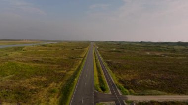 Mor bozkırlarla çevrili Danimarka kırsalını geçip Ringkobing Fjord ve Kuzey Denizi 'ne doğru giden düz bir yolda giden bir arabanın hava görüntüsü..