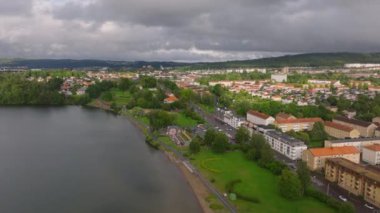 Bulutlu bir günde İsveç 'in bir kasabasında dolaşmak, sakin binalar, dingin bir göl ve yemyeşil alanlar sergiliyor, pitoresk bir şehir manzarası yaratıyor..
