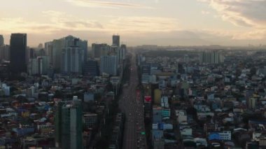 Manilas 'ın gün batımındaki canlı gökyüzü manzarası trafik ve gökdelenlerle dolu caddeleri ve yol kenarındaki alçak binaları aydınlatıyor..