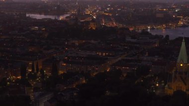 Stockholm ufuk çizgisi aydınlık binalar ve gün batımında canlı araba trafiği ile parıldıyor, çarpıcı, renkli bir gökyüzü ile çerçevelenmiş, şehirlerin cazibesini ön plana çıkarıyor..