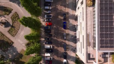 Hava manzarası, yol boyunca park halindeki arabaları ve kaldırımları kaplayan ağaçları gösteren, güneşli bir yaz gününde canlı bir şehir manzarası yaratan tipik bir Berlin caddesini vurguluyor..