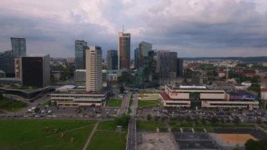 Kamera Vilnius, Litvanya 'daki modern ticaret bölgesini gösteriyor. Şehir manzarasında gökdelenler, ofis binaları ve yeşil alanlar yer alıyor..