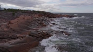 Turkuaz okyanus dalgaları Finlandiya 'nın Aland kentinde kayalık bir sahil şeridine çarpar. Dalgalar kıyıya vurduğunda beyaz deniz köpüğü havaya karışır..