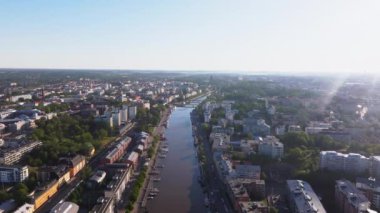 Güneş ışığı Turku şehir merkezini aydınlatır, Aura Nehri içinden geçerken onu aydınlatır. Çevresindeki binalar ve evler bu manzaralı Finlandiya şehrinde canlı bir şehir manzarası yaratıyor..