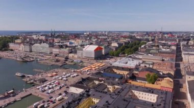 Hava manzaraları Helsinki 'nin canlı şehir merkezini vurguluyor, hareketli Pazar Meydanı' nı, Uspenski Katedrali 'ni ve güneşli bir gökyüzünün altında kabarık bulutlarla birlikte manzaralı Baltık Denizi' ni gösteriyor..