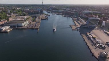 Hava görüntüleri Almanya 'da Kiel limanına yaklaşan bir feribotu yakalıyor ve suda beyaz bir iz bırakıyor. Sahne canlı deniz aktivitelerini ve manzaralı kıyı manzarasını gözler önüne seriyor.