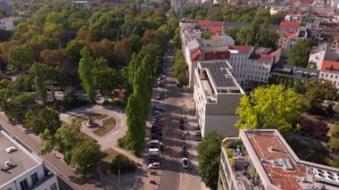 Berlin 'de yol kenarına park etmiş arabaların ve kavşağı ve heykeli olan bir şehir parkının hava görüntüsü..