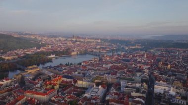 Prag şehrinin manzarası şafağın sıcacık ışığında parlıyor. Vltava Nehri şehrin içinden geçiyor, sabahın erken saatlerinde gökyüzünün yumuşak renklerini yansıtıyor..