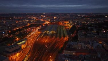 Prag ana tren istasyonunun hava manzarası alacakaranlıkta parlayan gölgelikleriyle, arabalar ve tren rayları istasyonun etrafını sararken.
