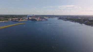 Güneşli bir yaz gününde Kiel Fiyort 'ta kameralar yankılanıyor. Görünüm, arka planında Kiel şehri ve büyük bir konteyner terminali olan limanı gösterir.