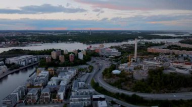 Stockholm şehri alacakaranlıkta ufuk çizgisinde. Arabalar yol boyunca köprüye doğru gidiyor, renkli gökyüzü suya yansıyor..