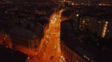 Aydınlanmış Prag sokakları, arabalar süzülürken ve tarihi binalar manzarayı çerçevelerken, gece hayatı ile titreşiyor, kentsel cazibe ve atmosferi vurguluyor..