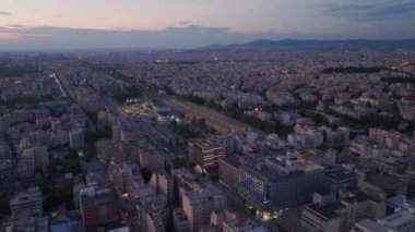 Yunanistan 'ın Selanik kentindeki Egnatia Bulvarı' nda arabalar yol alırken, binalar ve dağlar manzaralı bir zemin oluşturuyor. Sahne, alacakaranlıkta şehrin hareketli atmosferini yansıtıyor..