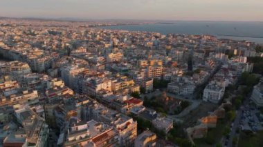 Selanik, Yunanistan, gün batımının ılık renklerinde parlıyor. Binalar ve sokaklar Ege Denizi 'ne yükseltilmiş bir perspektiften uzanırken şehir hayatı gelişiyor..