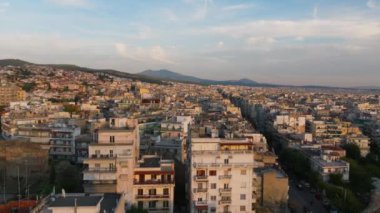 Yunanistan 'ın Selanik kenti, çağdaş mimari, işlek sokaklar ve açık mavi gökyüzünün altındaki uzak bir dağın karışımını gösteren canlı bir hava manzarası sunuyor.