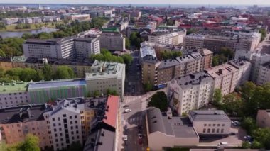 Helsinki, Finlandiya 'nın hava manzarasında canlı bir şehir manzarası sergilenmektedir. Kamera, bulutlarla dolu güneşli bir gökyüzünün altında modern ve geleneksel binaların bir karışımını gözler önüne seriyor..