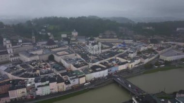 Salzach Nehri şehrin içinden geçerken, Avusturya 'nın Salzburg kentinin havadan görünüşü ön plana çıkıyor. Paneller, bulutlu bir gökyüzünün altında tarihi binalar ve modern cazibenin bir karışımını ortaya çıkarıyor..