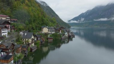 Hallstatt, Avusturya üzerinde dönen, bulutlu bir günde gölde yansıtılan büyüleyici bir köy sergileniyor. Tuhaf evler ve yemyeşil ağaçlar huzurlu ve huzurlu bir ortam yaratır..