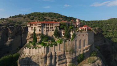 Güneş ışığı banyosu yapan Meteora manastırları nefes kesen mimarilerini vurguluyor, sakin ve tarihi bir Yunan manzarasında zarif bir şekilde yüksek kaya oluşumlarının tepesine tünemiş..